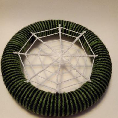 Complete white crochet spiderweb formed with radial lines and concentric rings on a green wreath