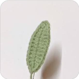 Two finished crocheted green leaves, with their stems wrapped in yarn.